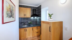 A compact kitchen with wooden cabinets, a black tiled backsplash, and a small window. - Lovely home in Aubenas (Aubenas)