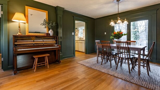 Un comedor con piano, sillas de madera, una mesa y una araña.
