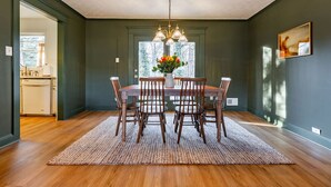 Comedor con una mesa de madera, seis sillas, una lámpara de araña y un ventanal con vistas a árboles.