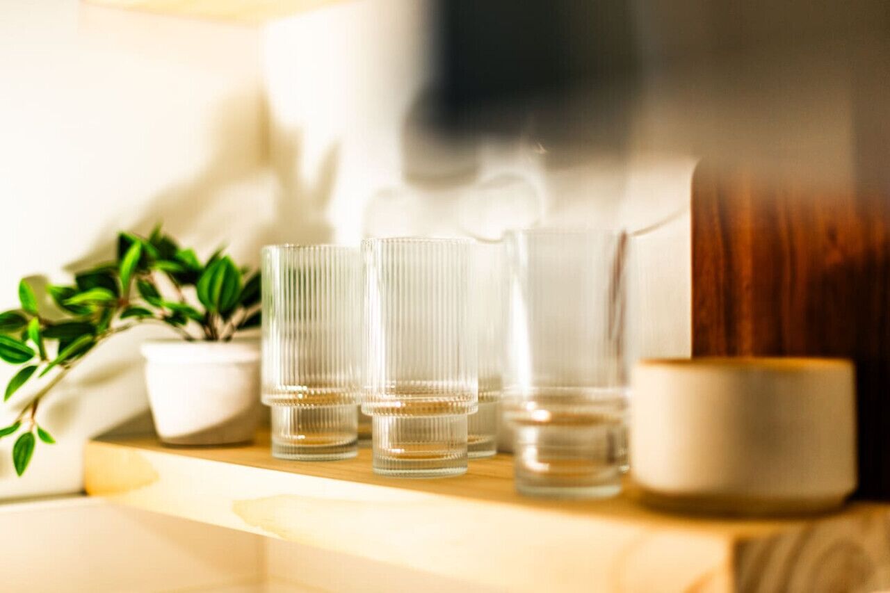 A wooden table with three clear glasses, a white candle, and a potted plant.