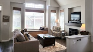 A living room with a sofa, armchair, TV, and windows with blinds. - Location Cottage - close to pools! 111 (Osoyoos)
