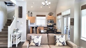 A modern interior with a sofa, kitchen, dining area, staircase, and a chandelier. - Location Cottage - close to pools! 111 (Osoyoos)
