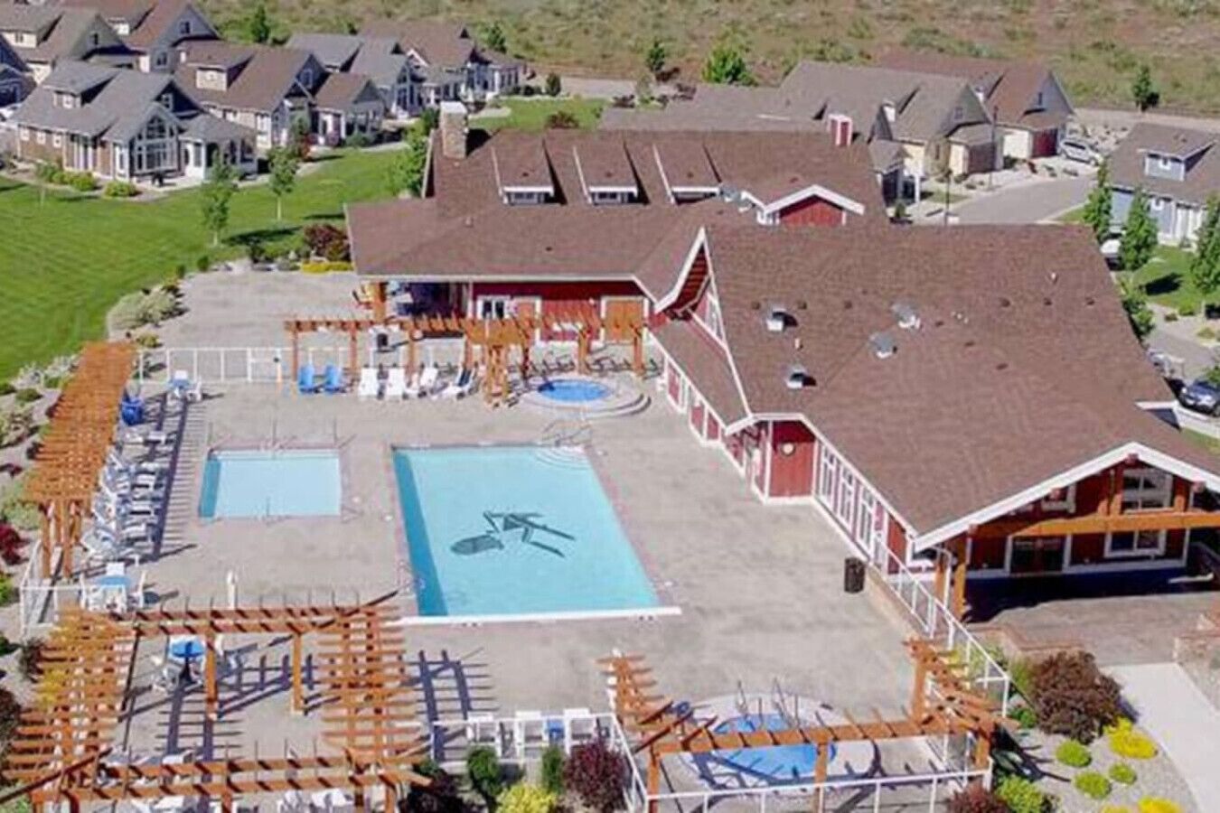 Un complexe hôtelier doté d’une grande piscine, de plusieurs espaces de détente et d’un bâtiment à la façade rouge.