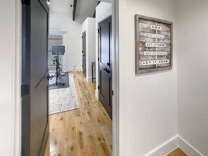 A hallway with wooden flooring, a gym area in the background, and a wall-mounted sign with 'LET IT SNOW' text.