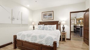 A bedroom with a wooden bed, two bedside lamps, a framed picture on the wall, and a view into a dining area. - Alpine Haven Retreat Ski-In Ski-Out Oasis Pool (Park City)