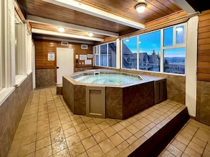 Un bain à remous dans une pièce aux murs en bois et au sol carrelé, une fenêtre avec vue et une porte sur laquelle est apposée une pancarte.