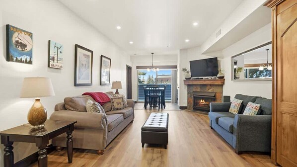 A living room with a sofa, ottoman, TV, fireplace, and framed pictures on the wall. - Alpine Haven Retreat Ski-In Ski-Out Oasis Pool (Park City)