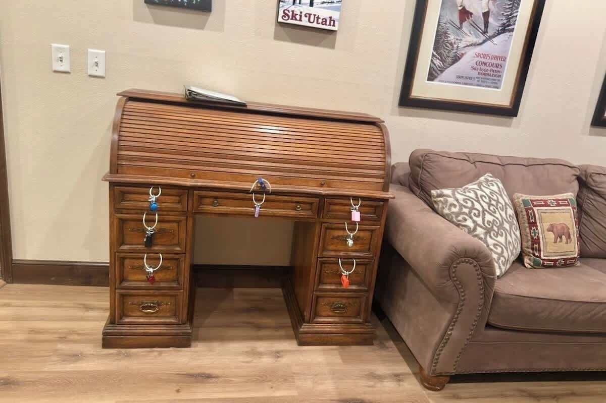 Een houten bureau met meerdere laden en ringen, een bruine leren bank met gestreepte kussens, en een muur met een ingelijste poster.