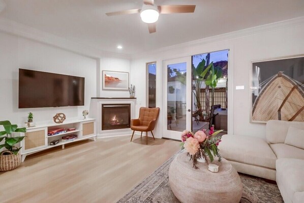 Una sala de estar moderna con una televisión de pantalla plana, chimenea, un sillón cómodo, un sofá y un ventanal con vistas al exterior.