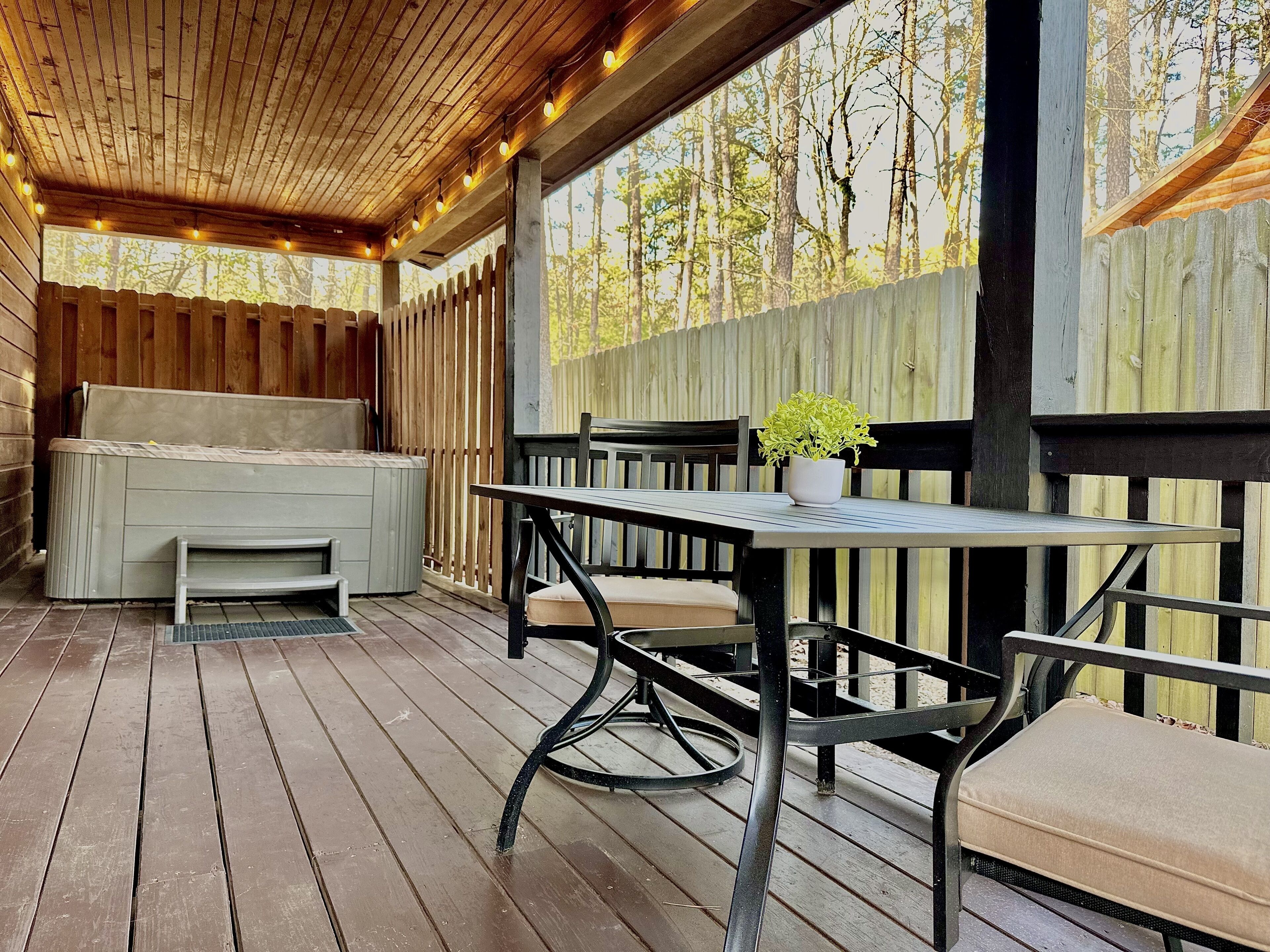 Eine Holzterrasse mit Tisch, Stühlen, einer Bank und einem Whirlpool.