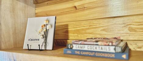 A wooden shelf with a book titled 's'mores' by Lisa Adams and 'Camp Cocktails: The Campout Cookbook' by the same author.
