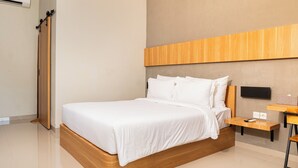 A modern hotel room with a wooden bed, a flat-screen TV mounted on the wall, and a small wooden nightstand. - Maluk Stay (Sumbawa Barat)