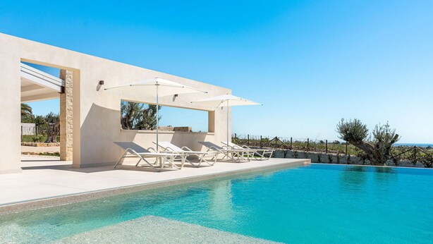 A modern pool area with clear blue water, white lounge chairs, and umbrellas.