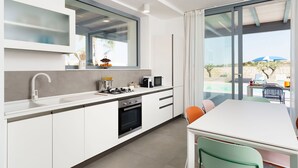 Ett modernt kök med ett stort fönster, en matplats med bord och stolar samt utsikt över en pool och grönområden utanför.
