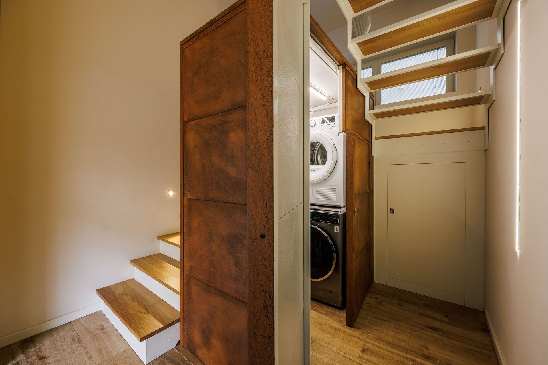 A laundry room with a washing machine and dryer, wooden steps leading to a door, and a small window above the dryer.