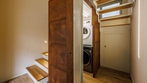 A laundry room with a washing machine and dryer, wooden steps leading to a door, and a small window above the dryer.