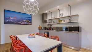 A modern kitchen with a dining area, featuring a cityscape painting, a unique light fixture, and a minimalist design.