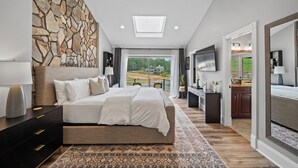 A bedroom with a stone wall, a bed, a TV, and a view of the outdoors. - Beautiful Waterfront Home w Hot Tub and great entertaining options! (Mooresville)