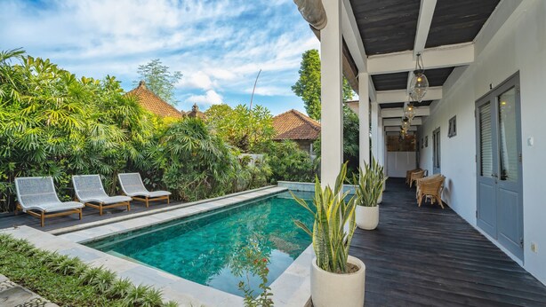 A pool area with lounge chairs, a wooden deck, and potted plants. - The Peacock Inn Ubud (Ubud)