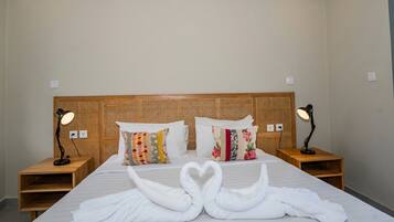 A neatly made bed with two pillows, a wooden headboard, bedside tables with lamps, and a heart-shaped towel arrangement.