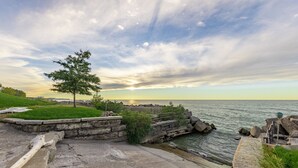 Une promenade en bord de mer, avec un sentier pavé de pierres, un arbre et une vue sur l’eau sous un ciel nuageux.