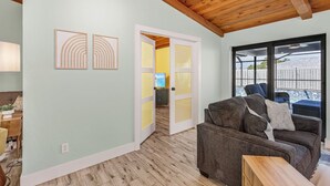 A living room with a wooden ceiling, a sofa, a coffee table, and a door leading to a kitchen. - Anchors Away - Pool with Spa - Garage Game Room (Cape Coral)