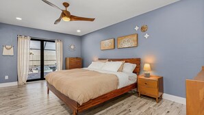 A bedroom with a wooden bed, a ceiling fan, a nightstand with a lamp, and a sliding glass door leading to an outdoor area. - Anchors Away - Pool with Spa - Garage Game Room (Cape Coral)