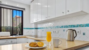 A modern kitchen with white cabinets, a wooden countertop, a coffee maker, a glass of orange juice, and a plate with croissants. - Adelfas 14 - Beach, Terrace, Pool, 2 Bedrooms (Torremolinos)