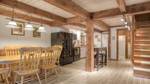 Une cuisine spacieuse avec des poutres en bois, un coin repas avec une table et des chaises en bois, et un réfrigérateur moderne.