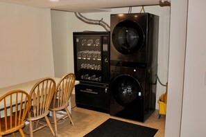 A compact room with a black washing machine, a small cabinet with hanging clothes, and a dining table with two chairs.