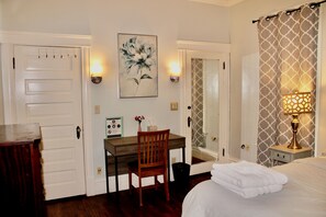 A hotel room with a bed, a desk, a chair, a painting, a mirror, and a lamp.