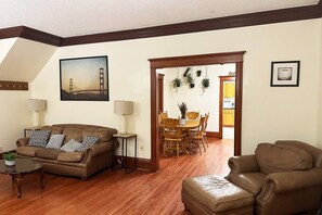 Uma sala de estar com um sofá de couro marrom, uma mesa de centro e um espaço de jantar com cadeiras de madeira e uma mesa.