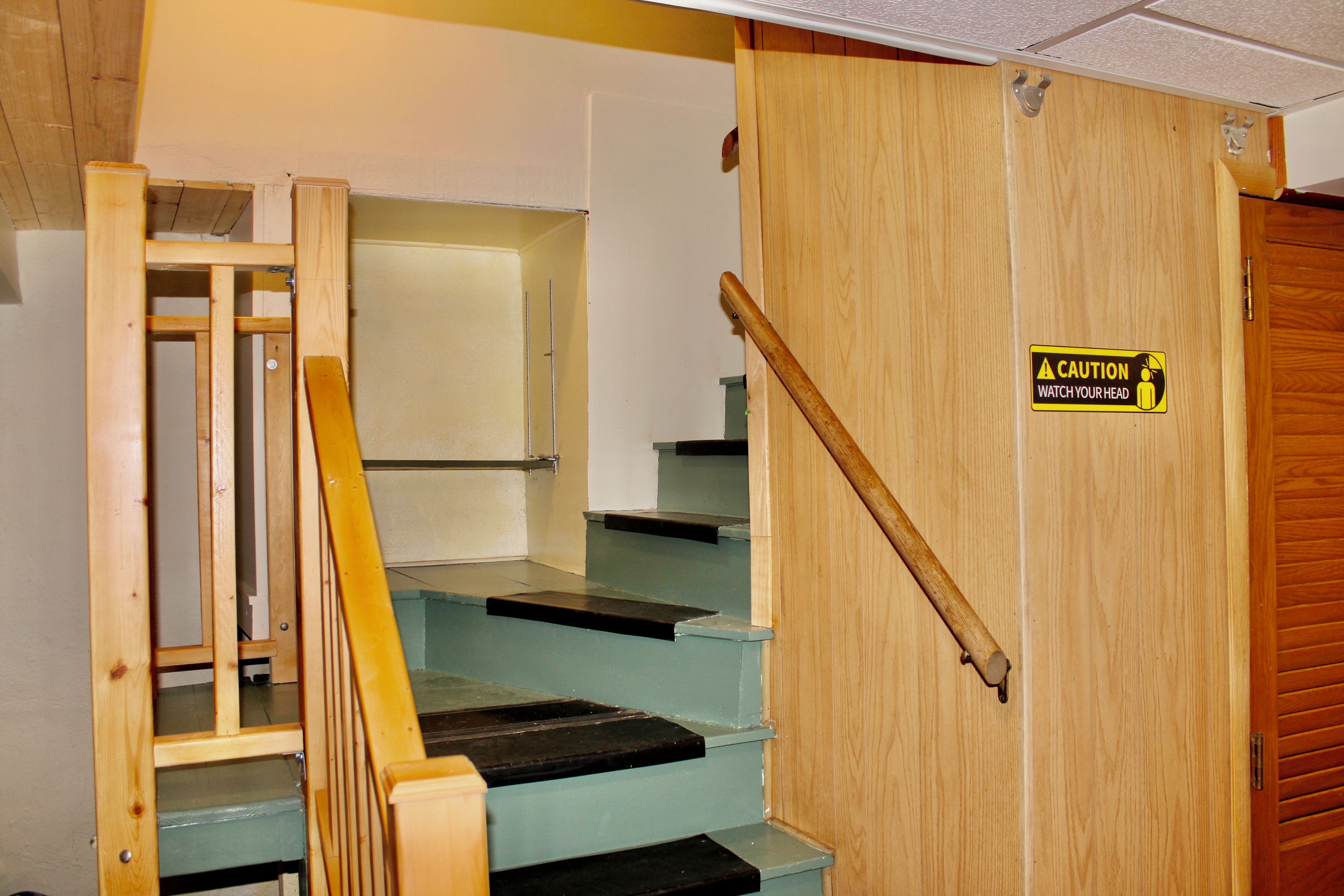 Eine Holztreppe mit einem Warnschild, einer teilweise geöffneten Tür und einer Metallhandläufe.