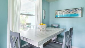 Un comedor con una mesa blanca, dos sillas, un cuenco de limones y un cuadro en la pared.