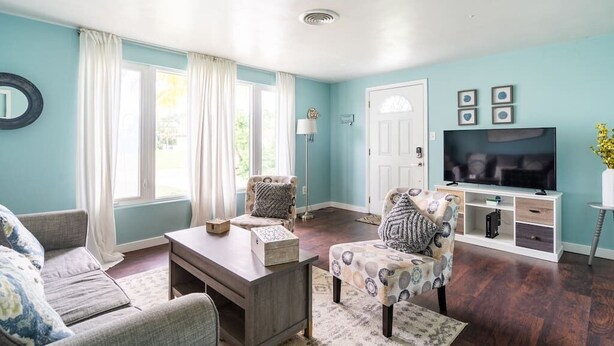 Una sala de estar con sofá, sillón, reposapiés, mesa de centro, mueble para la televisión y una puerta.