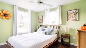 Un dormitorio con cama, ventilador de techo, mesita de noche, cómoda y obras de arte en las paredes.
