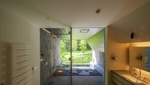 Une salle de bain moderne dotée d’une douche à parois de verre, d’un lavabo avec un plan de toilette en marbre et offrant une vue sur un jardin aménagé.