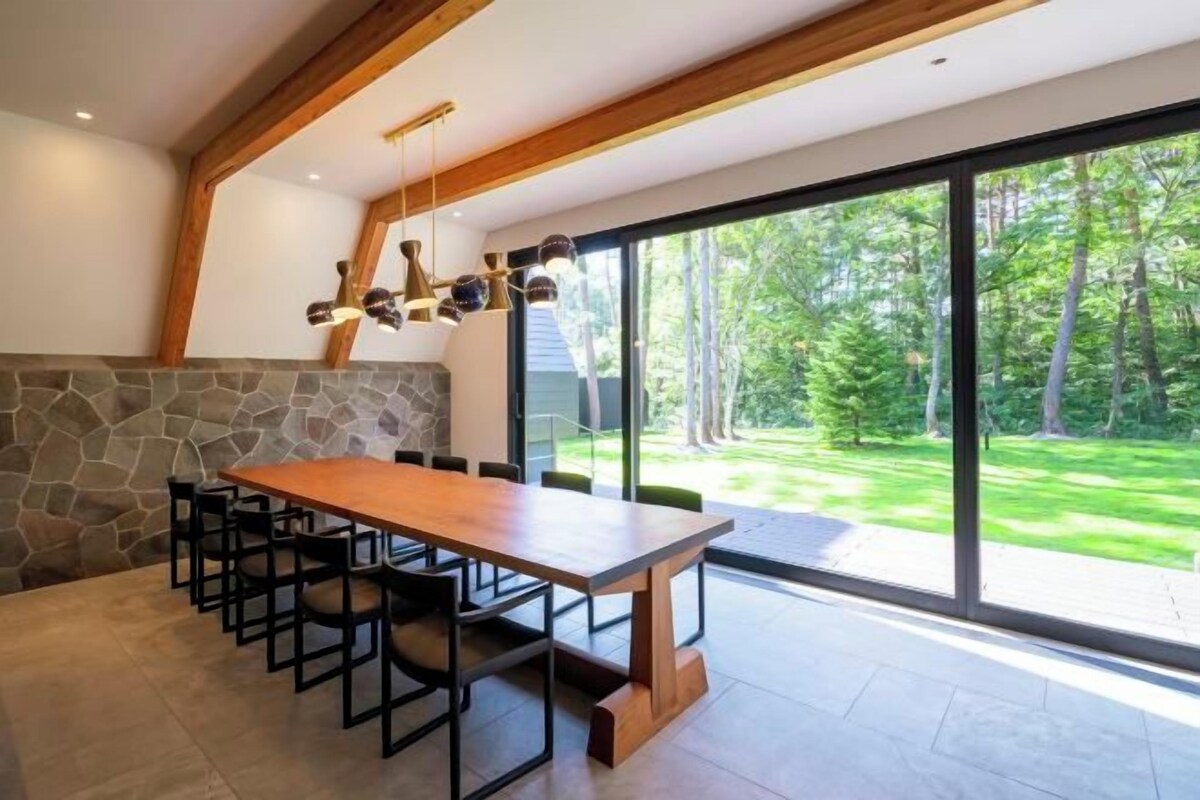 Ein moderner Essbereich mit einem großen Holztisch und Stühlen, einer Steinwand und großen Fenstern mit Blick auf einen üppigen Garten.