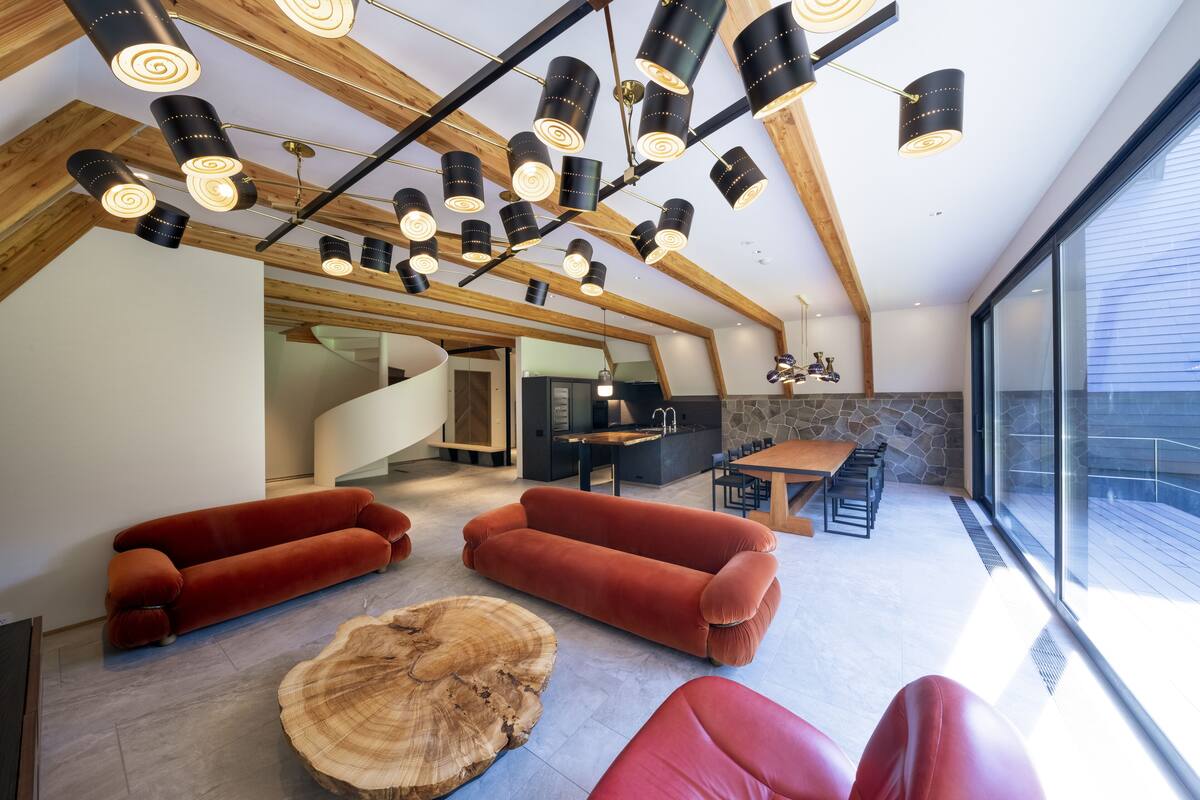 A modern interior with a wooden ceiling, red sofas, a dining area, and a large window.