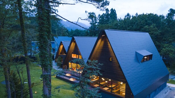Un hôtel moderne de style cabane, composé de plusieurs bâtiments à toits triangulaires, chacun doté de grandes fenêtres et d’espaces extérieurs aménagés pour se détendre.