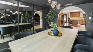 Uma área de jantar moderna com uma mesa comprida, cadeiras escuras e um vaso com plantas.