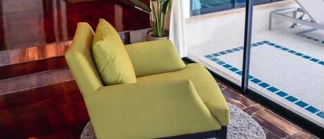 A modern room with a green sofa, a large window with a view of the sea, and a wooden floor.