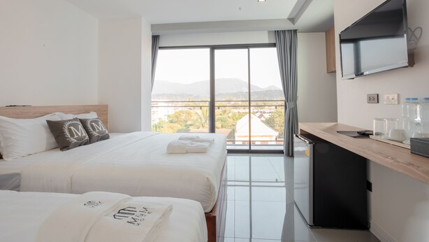 Habitación de hotel con dos camas, un televisor montado en la pared, una pequeña cocina y un amplio ventanal con vistas a la ciudad.
