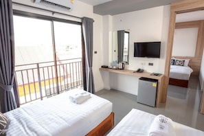 Ett hotellrum med två sängar, en TV, ett litet kylskåp, ett skrivbord med en spegel och en balkong med utsikt.