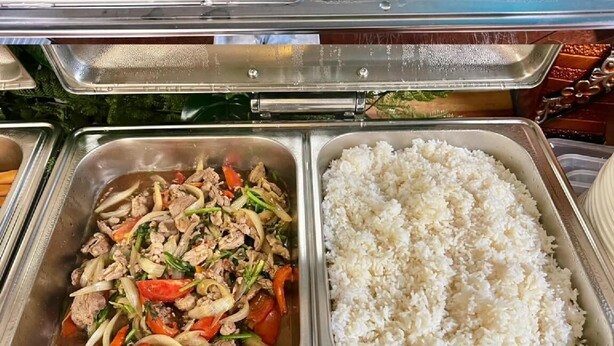 Un bufé con diversas opciones de comida, incluyendo huevos, salchichas, carne salteada y arroz.