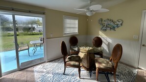 A dining area with a glass table and wooden chairs, a ceiling fan, and a view of a swimming pool.
