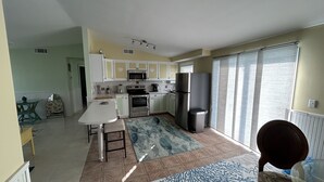 A compact kitchen with white cabinets, a microwave, stove, and a refrigerator. There is a dining area with a table and chairs.