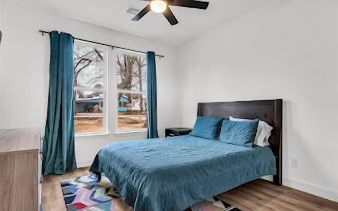 A bedroom with a bed, a nightstand, a window with curtains, and a ceiling fan.
