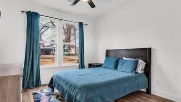 A bedroom with a bed, a nightstand, a window with curtains, and a ceiling fan.