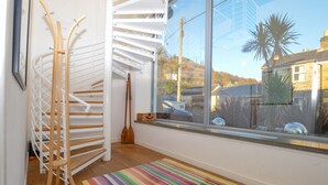 Ein Zimmer mit einer Wendeltreppe, einem großen Fenster mit Blick auf ein Haus und eine Palme sowie einem farbenfrohen Streifen Teppich auf dem Boden.